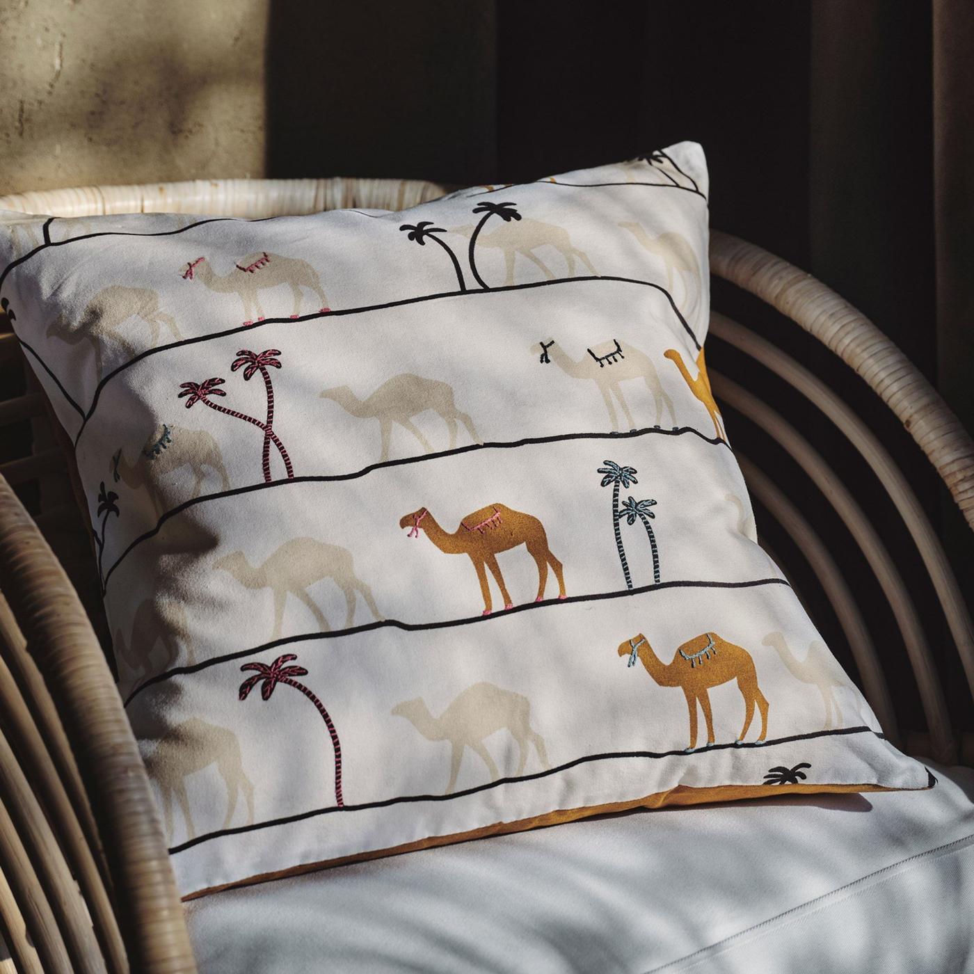 A rattan chair and a cushion with a white TILLTALANDE cushion cover with beige and brown hand-embroidered camels and palms.