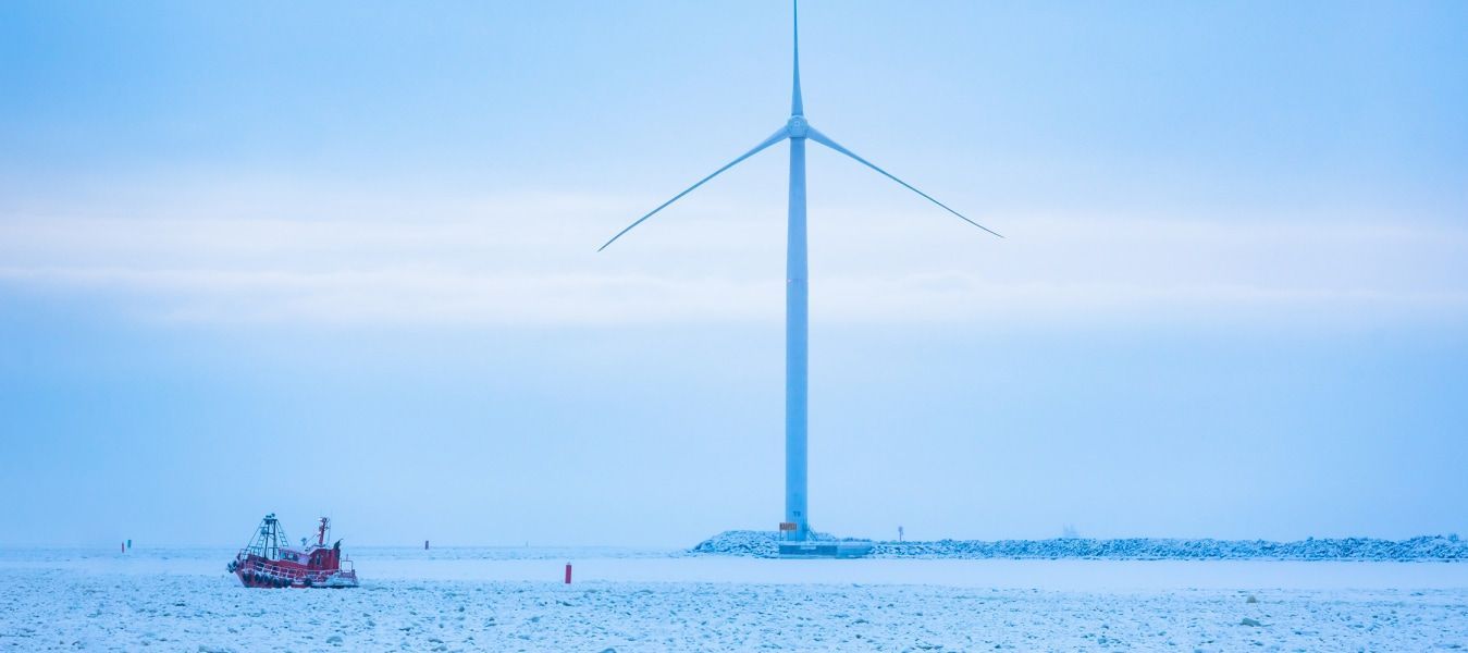 A white wind turbine is standing in a snowy environment with blue skies and clouds.