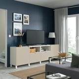 Moderan dnevni boravak: bijela BESTÅ TV jedinica sadrži TV ravnog ekrana i dekoracije. Mekani sivi jastuci i zavjese. Prirodni dekor s biljkama.