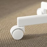 Krupni plan bijelog kotača uredske stolice na teksturiranom tepihu, prikazujući njegovu kvalitetu i dizajn.