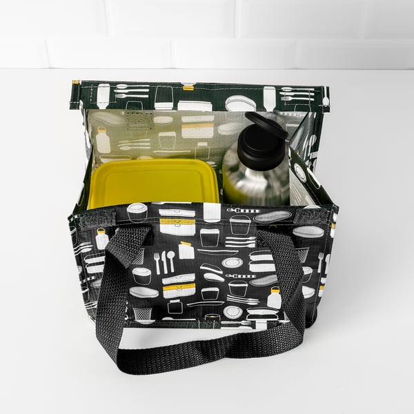 Otvorena crna torba s printom kuhinjskog pribora, koja sadrži žutu posudu i crnu bocu za vodu.