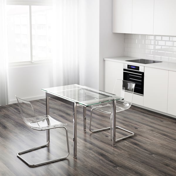 Moderna kuhinja s malim GLIVARP staklenim stolom i 2 prozirne stolice u blizini pećnice. Elegantan, minimalistički dizajn.