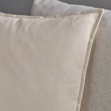 Navlaka za jastuk s križnim šavovima, svijetla bjelokost, mekana na dodir, zatvaranje patentnim zatvaračem, naslonjena na teksturiranu površinu.