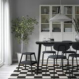 Moderna blagovaonica s crnim stolicama, stolicama, drvenim stolom, tepihom, svjetiljkom, policama s knjigama i biljkom u saksiji.