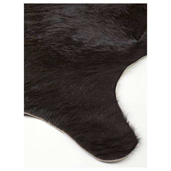 Crni tepih od kravlje kože s prirodnom teksturom i malim varijacijama u boji, prikazan na bijeloj pozadini.