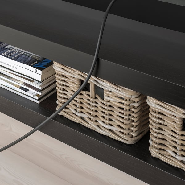 CRNI minimalistički TV stalak s tkanim košarama i složenim knjigama. Vidljivo upravljanje kabelima.
