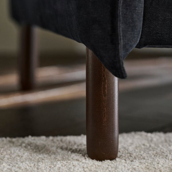 Tamna sofa s elegantnim drvenim nogama, koja pokazuje kvalitetan dizajn i udobnost.