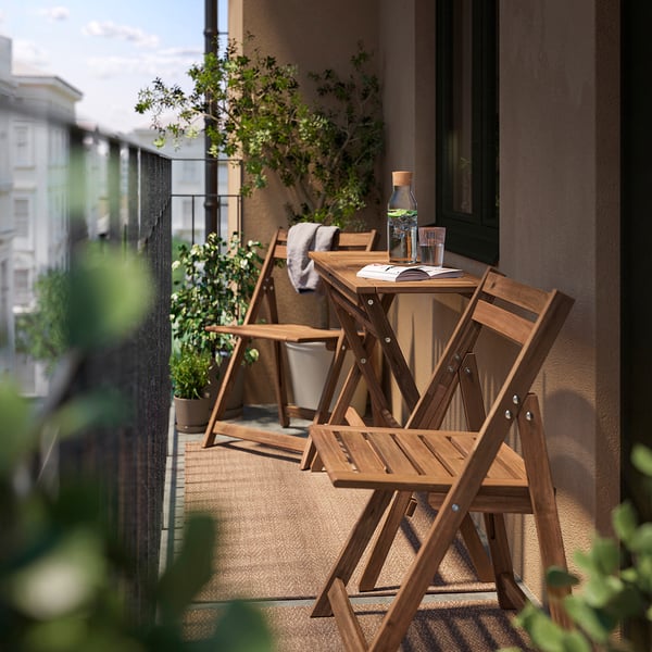 Mali balkon s drvenim stolom i stolicama, zelenim biljem i pogledom na grad.