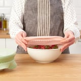 Osoba koja stavlja svijetlo ružičasti poklopac zdjele na bijelu zdjelu s jagodama na drvenom stolu.