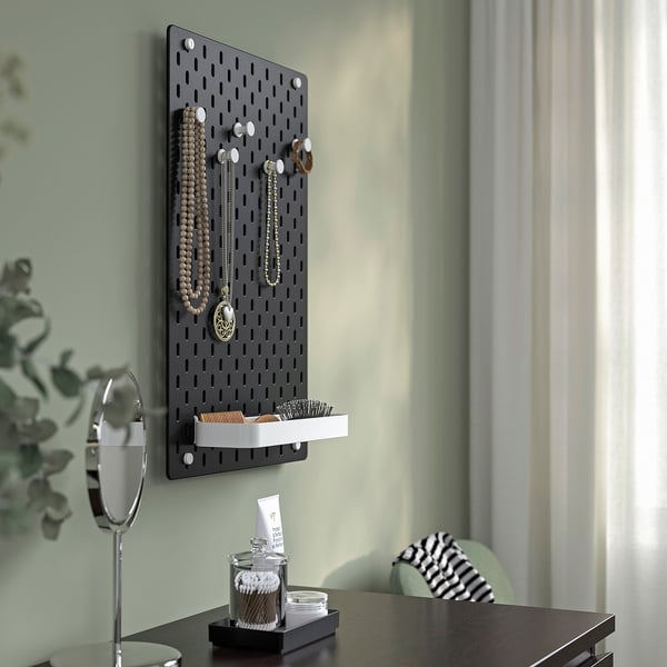 SKÅDIS pegboard drži nakit, četke, pamučne štapiće. Zeleni zid, biljka.