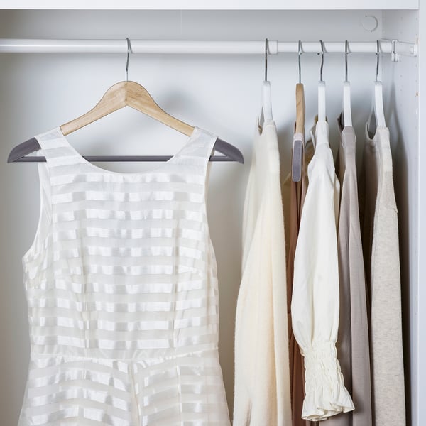 Ormar s drvenim vješalicama. Lijeva vješalica drži bijelu haljinu bez rukava. Desni dio sadrži nekoliko odjevnih predmeta svijetle boje.