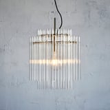 Moderni luster s prozirnim staklenim cilindrima visi na metalnoj kuki, emitirajući toplu svjetlost.