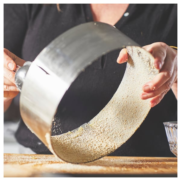 Osoba koristi okrugli, podesivi okvir za pečenje od nehrđajućeg čelika na drvenoj površini za pečenje ili rezanje kolača.