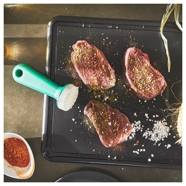 Crni pladanj sa sirovim mesom začinjen začinima. Tu je zeleni alat za omekšavanje i mala posuda s crvenim začinom.