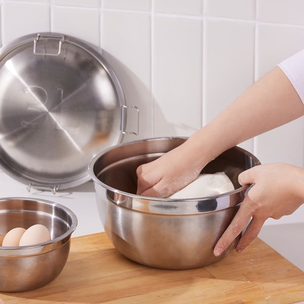 A tészta keverése egy nagy rozsdamentes acél tálban, amely a helytakarékosság érdekében hasonló tálakkal fészkelődik. Fém fedelek a közelben élelmiszerek tárolására.