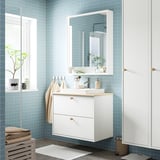 Modern fürdőszoba FAXÄLVEN fehér tükörszekrényrel, nagy tükörrel, tárolóval, világítással és függő törölközőkkel.