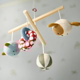 Négy színes játék lóg egy fakereten, amelyek célja, hogy felkeltsék a baba látását és kíváncsiságát a pelenkacsere során.