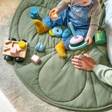 Egy gyerek játékokkal játszik egy kerek, steppelt takarón a padlón.