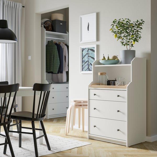 Modern nappali HAUGA fehér ládával, fekete székekkel, növényekkel és műalkotásokkal.