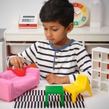Fiatal fiú játszik a HUSET játékbaba bútorkészlettel, és miniatűr IKEA ihlette darabokat rendez el.