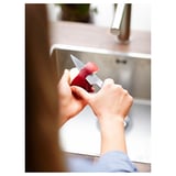 Kezek hámozzák a vörös almát egy kis késsel a mosogató közelében.