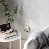 Minimalista lakótér kisasztallal, vázával, könyvekkel és akkumulátorral. A személy válla látható.