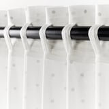 A fekete függönyrúd három fehér függönyt tart hurkolt kötésekkel és pontozott mintákkal, lehetővé téve a fény átszűrődését, miközben magánéletet biztosít.