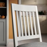 Közeli kép egy stílusos, kiváló minőségű fehér fa székről, függőleges rácsos háttámlával és kárpitozott üléssel.