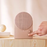 Kézzel érintő gomb a bézs színű bluetooth hangszórón a fa polcon.