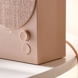 Közeli kép egy stílusos, kiváló minőségű bézs színű bluetooth hangszóróról, texturált szövetborítással és érintőképernyőkkel.
