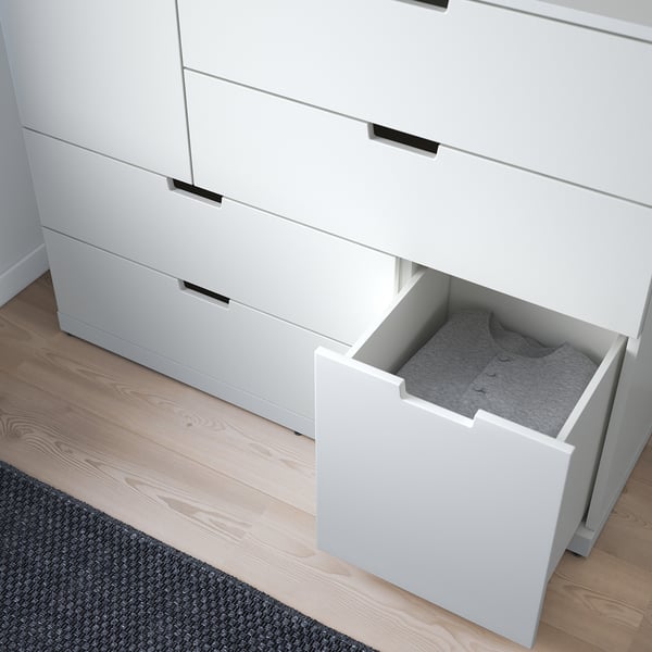 Fehér komód nyitott fiókkal, szürke szövet tartalmát felfedve világos fapadlón.
