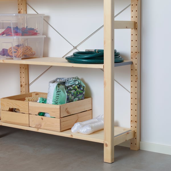 Világos fa tárolópolcok átlátszó edényekkel, amelyek színes tárgyakat tartalmaznak, beleértve a zöld tömlőt és a műanyag zacskókat az alsó polcon.