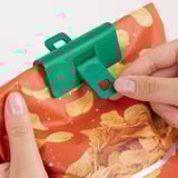 A kezek zöld pecsétkapoccsal zárják le a snack zacskót. A klip a burgonya chips zacskójának rögzítését mutatja, frissen tartva a tartalmat.