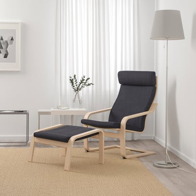 Minimalista lakótér kék POÄNG fotelrel, hozzáillő lábtartóval, lámpával és növénnyel. A világos falak és a bézs szőnyeg hangulatos légkört teremtenek.