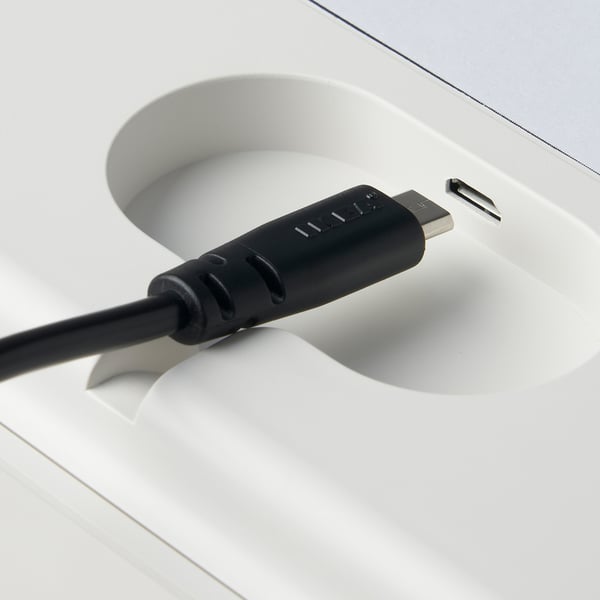 Fekete usb-kábel fehér töltőtálcához csatlakoztatva a PRAKTSPIREA akkumulátorral működő lámpákhoz.