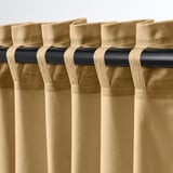 Bézs színű bársonyfüggönyök közeli képe fekete rúdon, redőzött puha redők, elegáns textúra.