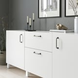 Fehér szekrény antik fogantyúkkal, dekorációs tárgyakkal, köztük gyertyatartókkal és könyvekkel.