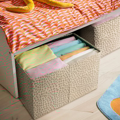 SLÄKT tárolódoboz, bézs szürke pöttyökkel, összehajtogatott takarók tárolására. Kisebb, mint az ágy, amely alá illeszkedik, fogantyúkkal a könnyű használat érdekében.