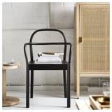 Modern fekete étkezőszék köteg könyvvel, fából készült szekrény és kis asztal mellett, átlátszó üveggel.