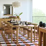 Modern étkező narancssárga-kék szőnyeggel, fából készült asztallal, székekkel, csillárral, tükörrel és természetes fénnyel.