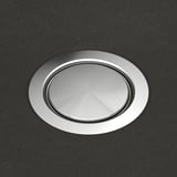 Fényes rozsdamentes acél lefolyófedél egy síkban a sötét munkalappal, körkörös mintázatban visszaverve a fényt.