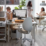 Modern munkaterület három nővel. Ketten ülnek a TROTTEN íróasztaloknál, a másik étellel.