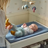 Nő kiságyba helyezi a babát macskahuzattal és játékokkal.