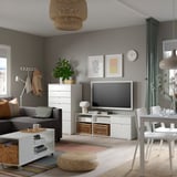 Modern nappali szürke falakkal, fehér VIHALS tv-asztallal, szürke kanapéval, csíkos szőnyeggel és szőtt függőlámpával.