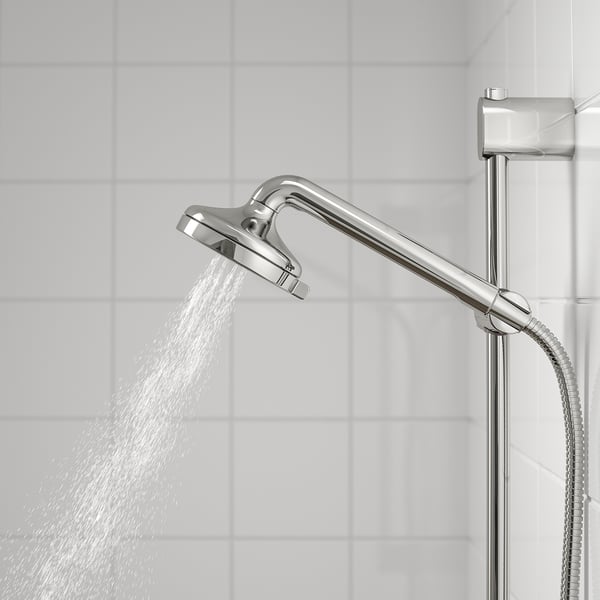 Króm zuhanyfej teljes permetezéssel, csúszórúdra szerelve, fehér csempékhez állítva.