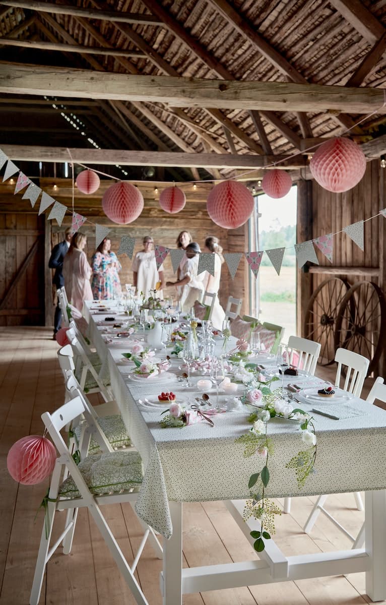 Rustic barn with a long decorated dining table, pink lanterns, and guests gathered at the far end.