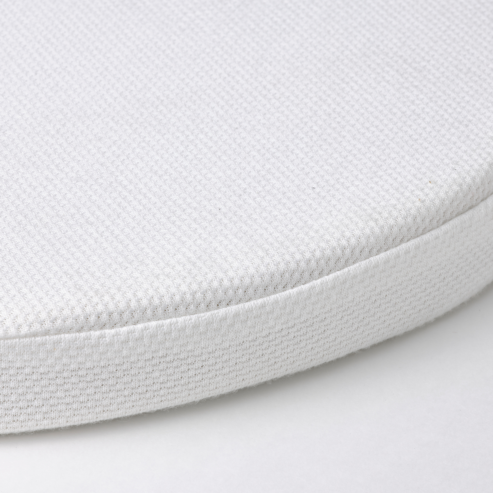 Close-up of a firm, white bassinet mattress with a textured cover, showing quality and comfort.