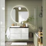 Modern white bathroom with glossy round mirror, floating cabinet, marble basin, and plants. Spacious & sleek.