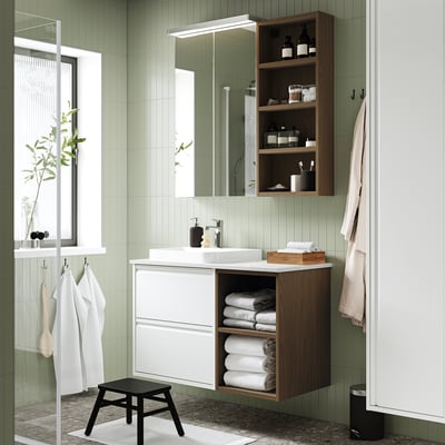 Modern bathroom with white & wood cabinet, mirror, sink, towels, and stool. Green tiled walls, large window.