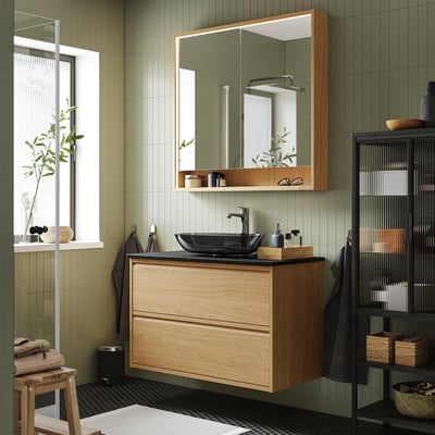 Modern bathroom with ÄNGSJÖN oak vanity, wall-mounted drawers, dark grey sink, large mirror, and open shelf with towels.